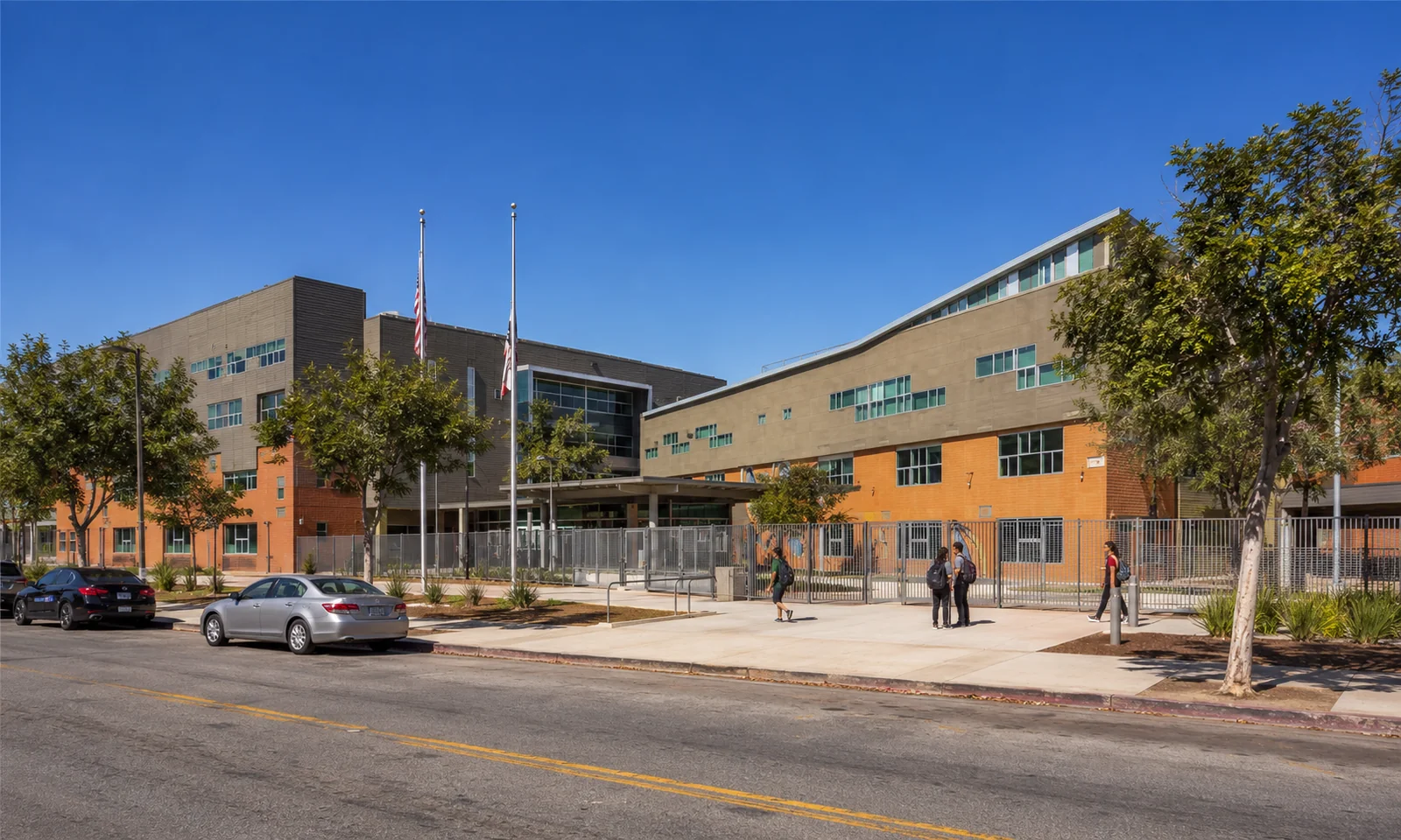 South Central Los Angeles High School No. 1. The main classroom and administration building at the campus entrance, framed by street trees and flagpoles. LAUSD build-to-suit campus.