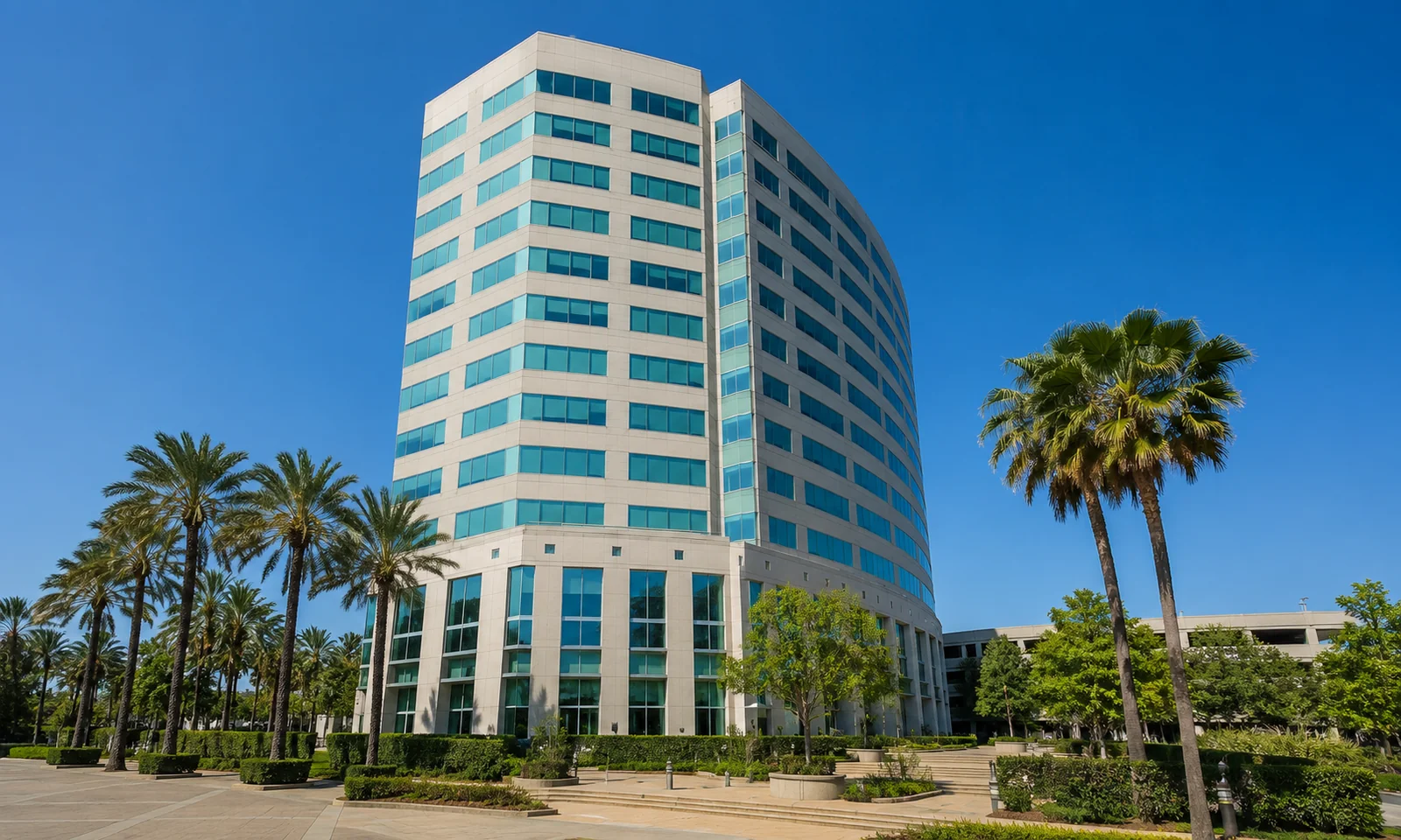 Stadium Towers Plaza Anaheim. The twelve-story curved Class A office tower framed by palm trees under clear sky. Orange County Class A office.